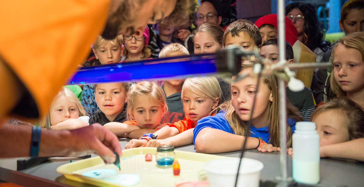 This image shows children around a table watching a science demo. Kids activities like this one happen every day at Science City.